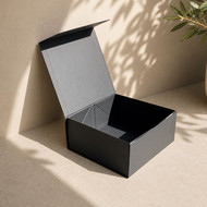 Boîte cadeau carrée noire ouverte sur un fond beige ensoleillé